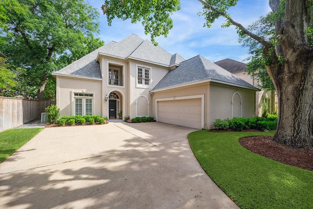 view of front of property with fence, an attached garage, stucco siding, a shingled roof, and concrete driveway