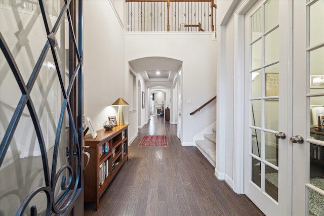 entryway featuring french doors, a towering ceiling, dark wood-type flooring, arched walkways, and stairway