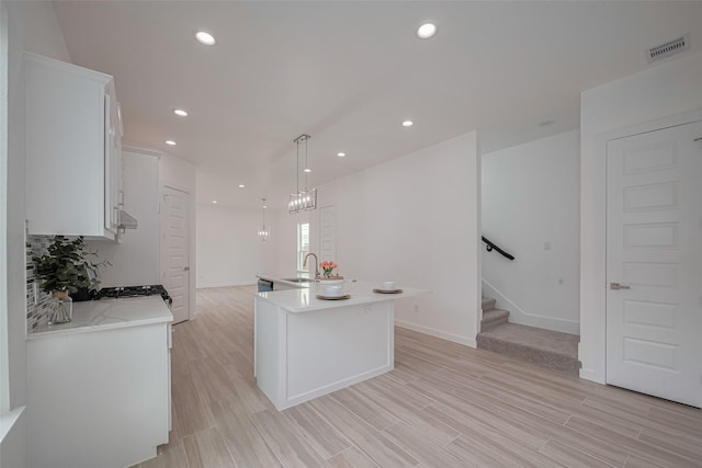7307 W Knoll St, Houston, TX 77028 - kitchen featuring light wood-style flooring, a sink, a kitchen island with sink, white cabinetry, and light countertops