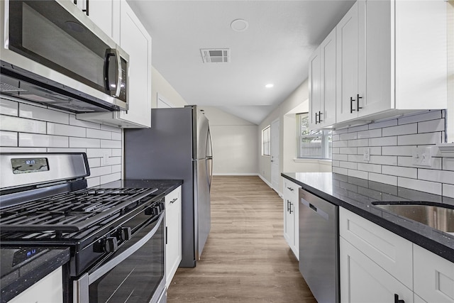 6727 Winding Trace Dr, Houston, TX 77086 - kitchen with stainless steel appliances, light wood-type flooring, vaulted ceiling, white cabinets, and baseboards