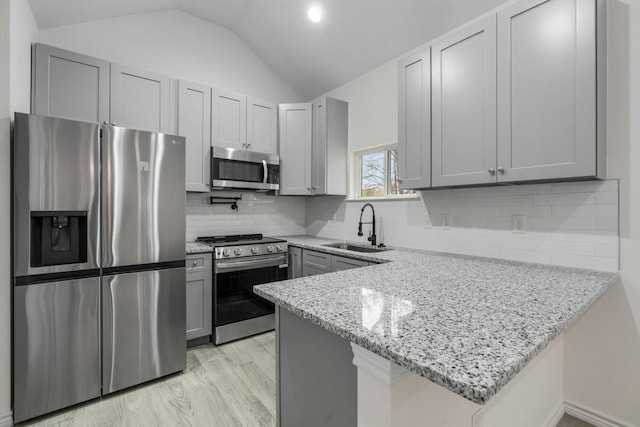 kitchen with a peninsula, a sink, stainless steel appliances, light stone counters, and lofted ceiling
