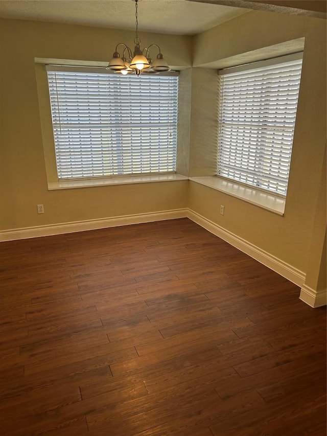 unfurnished room with baseboards, an inviting chandelier, and dark wood-style floors