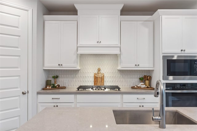 318 Mistletoe Ridge Ct, Montgomery, TX 77316 - kitchen featuring under cabinet range hood, a sink, white cabinetry, decorative backsplash, and stainless steel appliances