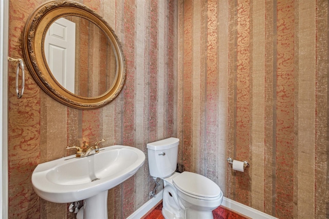 bathroom with toilet, wood finished floors, a sink, wallpapered walls, and baseboards