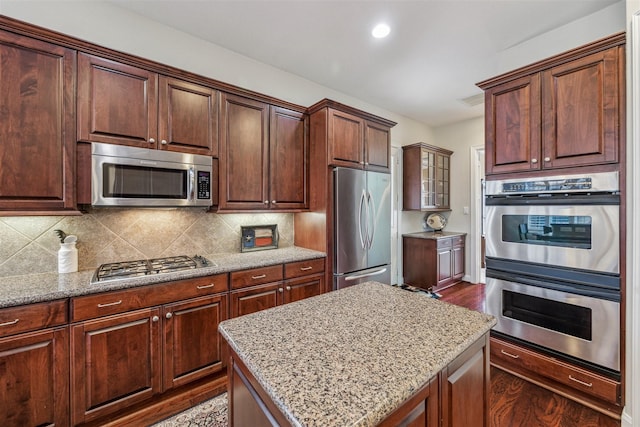 kitchen featuring stainless steel appliances, light stone countertops, decorative backsplash, dark wood-style floors, and recessed lighting