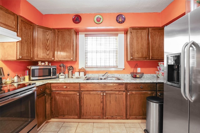 kitchen featuring appliances with stainless steel finishes, brown cabinetry, light tile patterned flooring, and a sink
