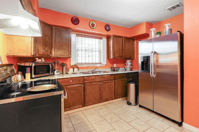 kitchen with under cabinet range hood, brown cabinetry, a sink, and appliances with stainless steel finishes
