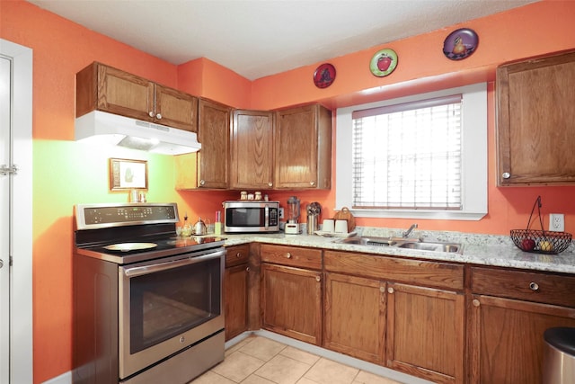 kitchen featuring light tile patterned floors, brown cabinets, a sink, stainless steel appliances, and under cabinet range hood