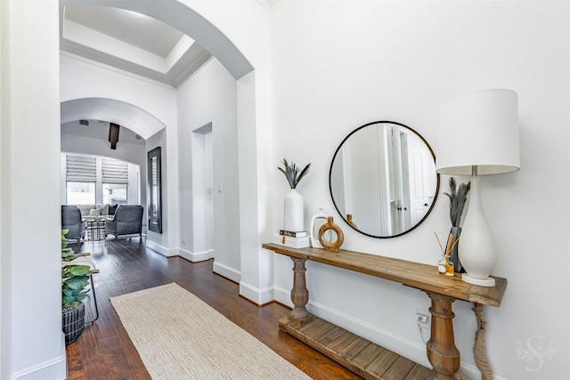 foyer entrance featuring arched walkways, baseboards, wood finished floors, and crown molding