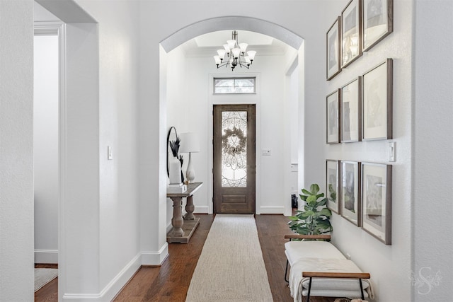 foyer with arched walkways, dark wood-style floors, a chandelier, ornamental molding, and baseboards