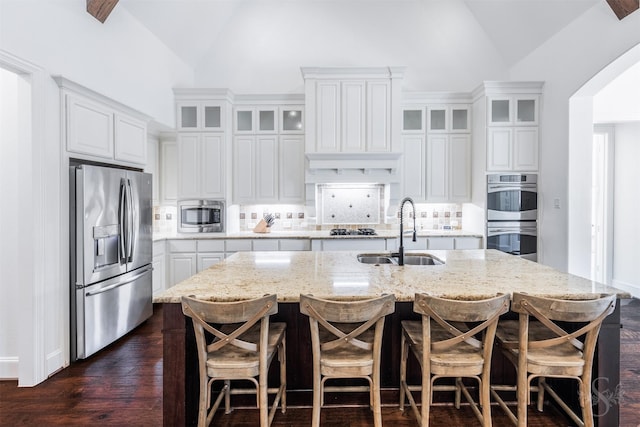 kitchen featuring appliances with stainless steel finishes, a sink, tasteful backsplash, an island with sink, and white cabinets