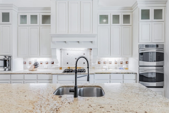 kitchen with stainless steel appliances, a sink, white cabinets, and glass insert cabinets