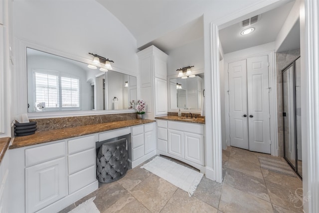 full bath featuring a stall shower, vanity, stone tile floors, and vaulted ceiling