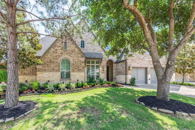 tudor home with brick siding, stone siding, driveway, a front yard, and roof with shingles