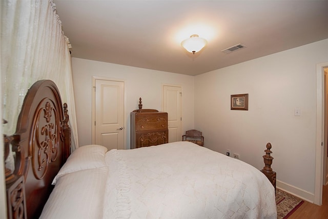 bedroom with baseboards, visible vents, and wood finished floors