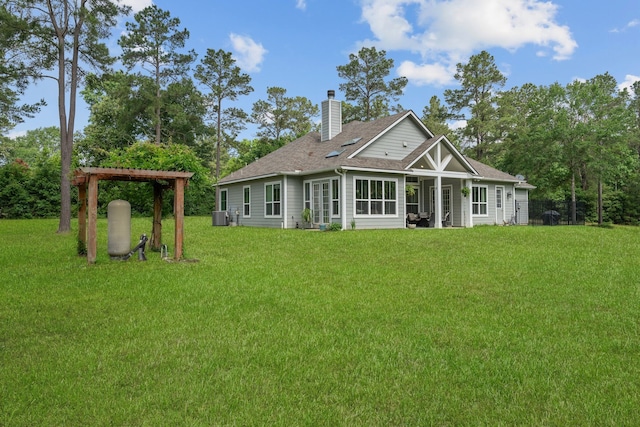 back of house with a chimney, a yard, and a shingled roof