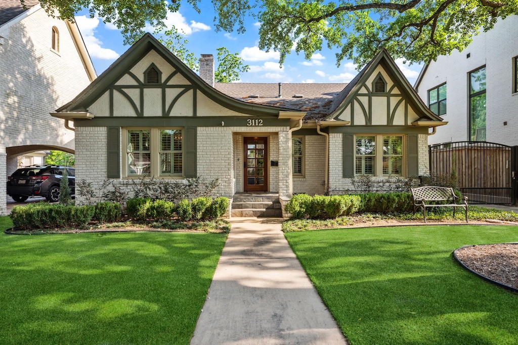 tudor house with brick siding, stucco siding, a chimney, and a front yard