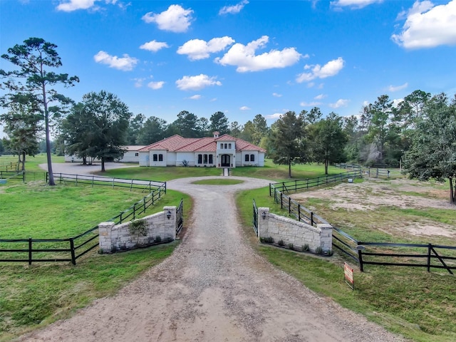 view of property's community with a lawn, a rural view, fence, and curved driveway
