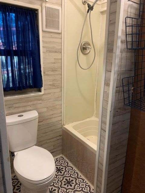 415 5th St, San Leon, TX 77539 - bathroom with tile patterned floors, toilet, visible vents, and wooden walls