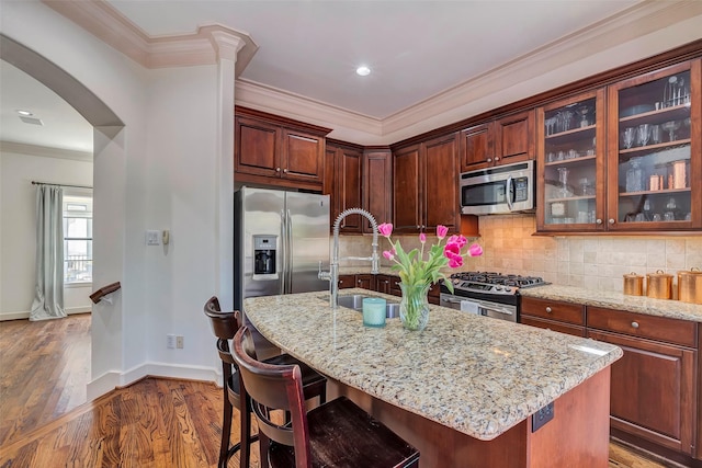 kitchen with wood finished floors, ornamental molding, light stone counters, arched walkways, and appliances with stainless steel finishes