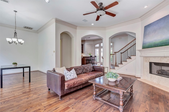 living area featuring light wood-style flooring, ceiling fan with notable chandelier, a premium fireplace, crown molding, and visible vents