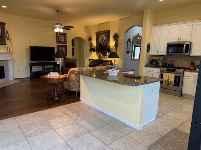 kitchen featuring arched walkways, white cabinets, appliances with stainless steel finishes, and dark stone counters