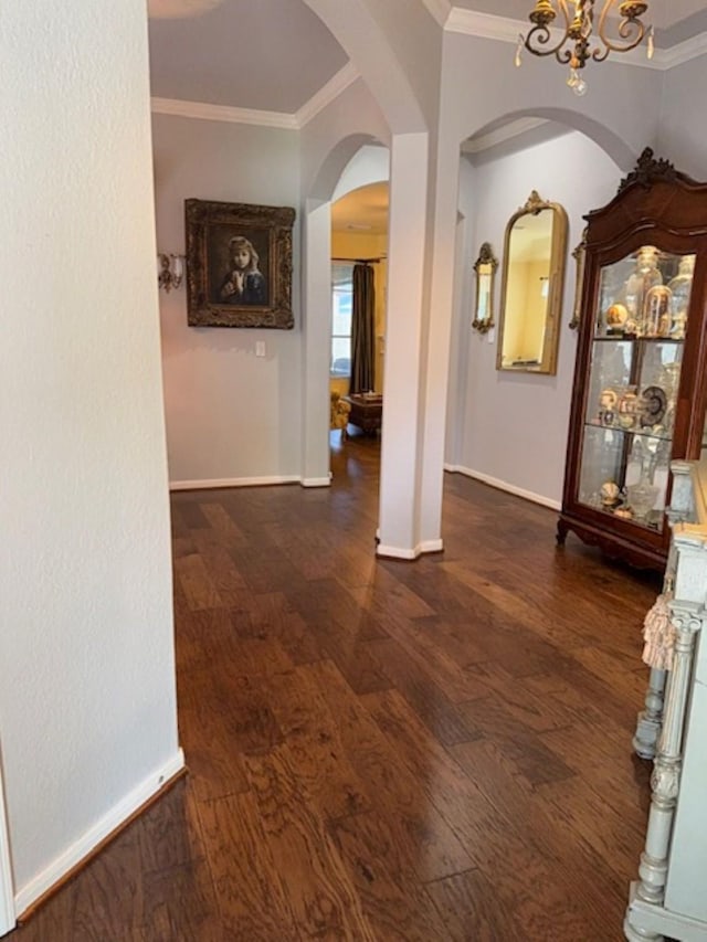 hallway featuring crown molding, arched walkways, dark wood-style floors, and a notable chandelier