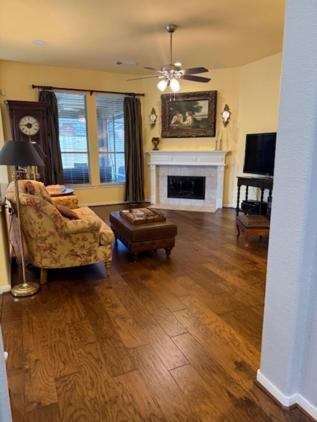 living area featuring a tile fireplace, baseboards, a ceiling fan, and wood finished floors