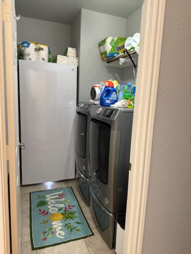 clothes washing area featuring washing machine and dryer, laundry area, and light tile patterned flooring
