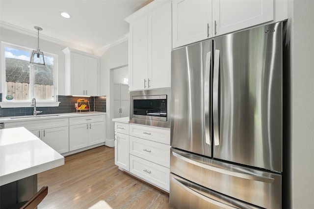 kitchen featuring appliances with stainless steel finishes, a sink, crown molding, light countertops, and white cabinetry