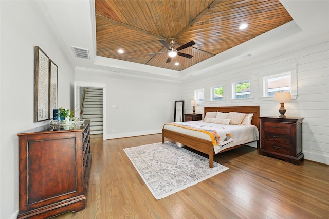 bedroom with a tray ceiling, wooden ceiling, light wood-style floors, baseboards, and ceiling fan