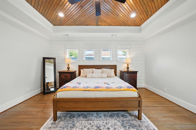 bedroom with a tray ceiling, wood ceiling, crown molding, baseboards, and wood finished floors