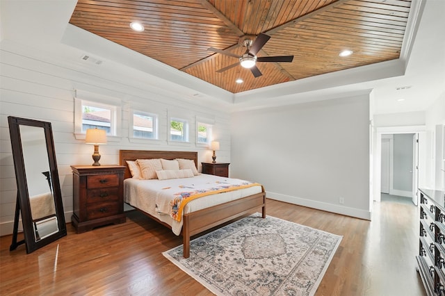 bedroom with a tray ceiling, wood ceiling, light wood finished floors, baseboards, and ceiling fan