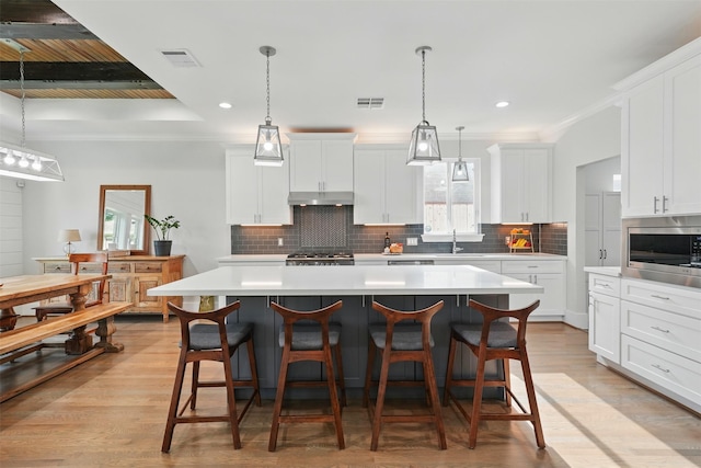 kitchen featuring stainless steel microwave, a center island, light countertops, decorative backsplash, and white cabinets