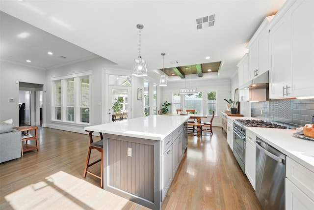 kitchen with stainless steel dishwasher, light wood finished floors, under cabinet range hood, a kitchen bar, and recessed lighting