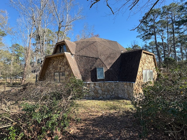 view of property exterior with a shingled roof and stone siding