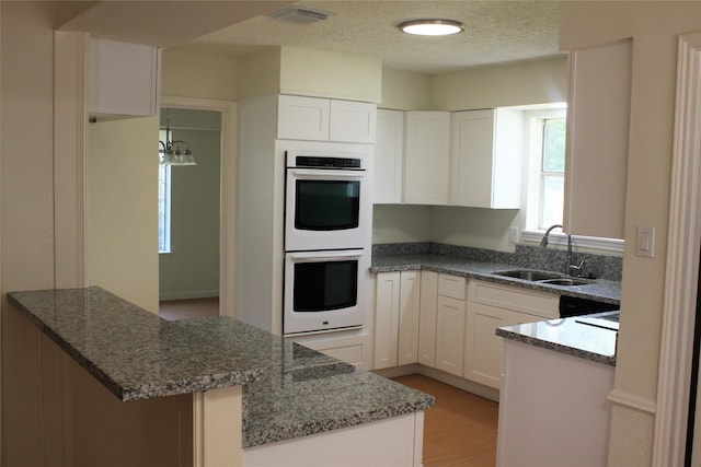 6103 Portal Dr, Houston, TX 77096 - kitchen with white double oven, a sink, white cabinets, dark stone counters, and a textured ceiling