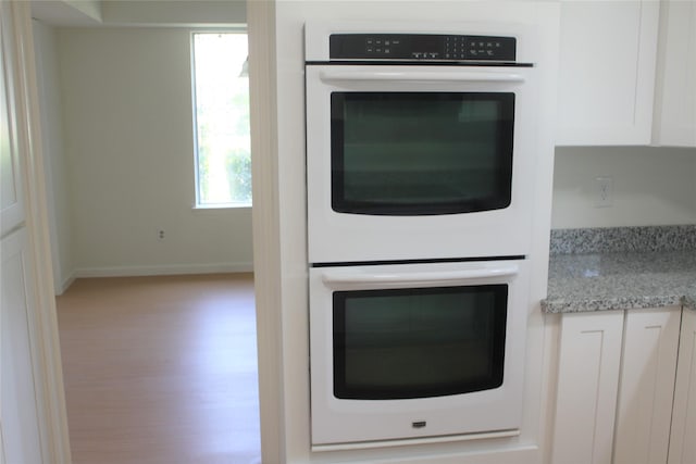 6103 Portal Dr, Houston, TX 77096 - kitchen view of double oven, white cabinets, light stone counters, baseboards, and wood finished floors