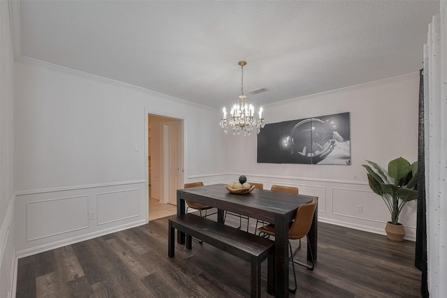 dining room featuring a chandelier, dark wood-style flooring, crown molding, a decorative wall, and a wainscoted wall