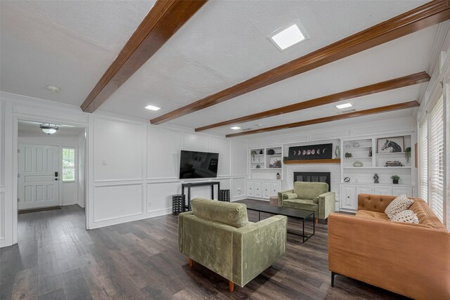 living area featuring a glass covered fireplace, beam ceiling, dark wood-style flooring, crown molding, and a decorative wall