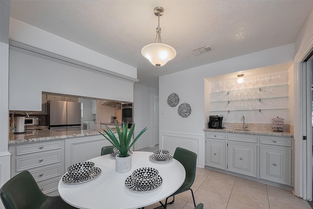 dining area with wet bar, light tile patterned flooring, wainscoting, and a textured ceiling