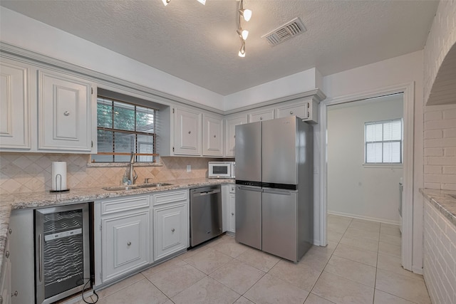 kitchen featuring appliances with stainless steel finishes, wine cooler, a sink, decorative backsplash, and light tile patterned floors
