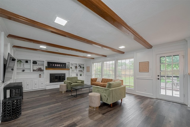 living room featuring beam ceiling, dark wood finished floors, a fireplace, a decorative wall, and a textured ceiling