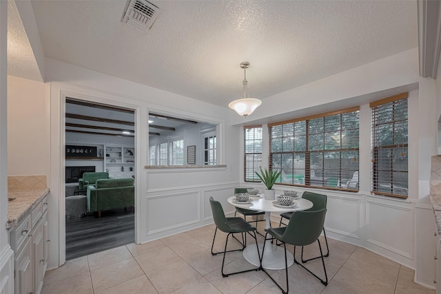 dining space with a decorative wall, light tile patterned floors, a textured ceiling, a wainscoted wall, and a fireplace