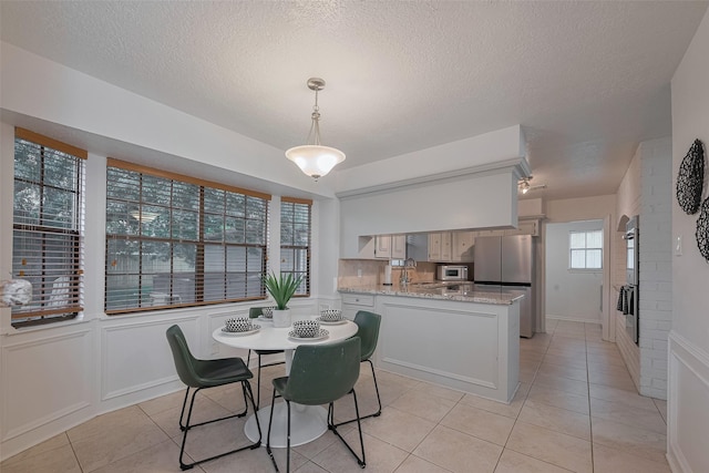 dining space featuring light tile patterned flooring, a textured ceiling, and wainscoting