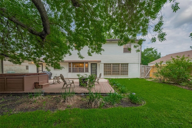 back of property with a hot tub, brick siding, a wooden deck, and a gate