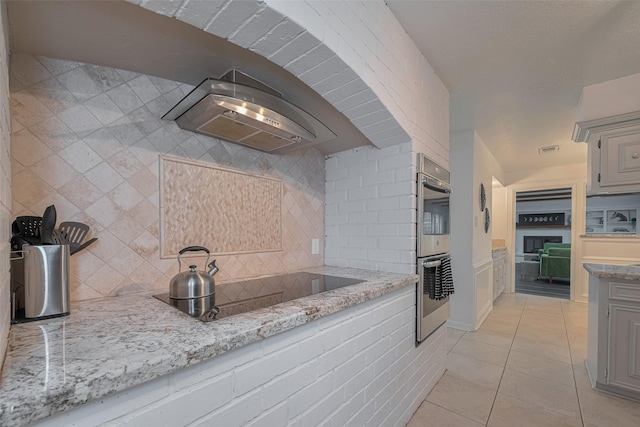 kitchen featuring black electric stovetop, wall chimney range hood, light tile patterned flooring, backsplash, and stainless steel double oven