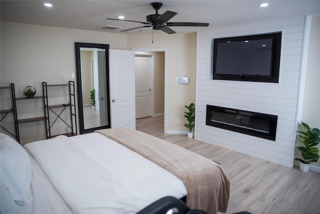 bedroom featuring a large fireplace, light wood-style flooring, baseboards, and recessed lighting
