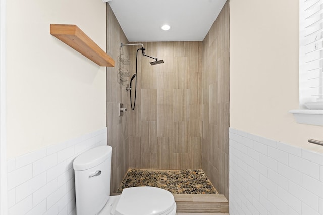 full bathroom featuring toilet, tiled shower, a wainscoted wall, tile walls, and recessed lighting