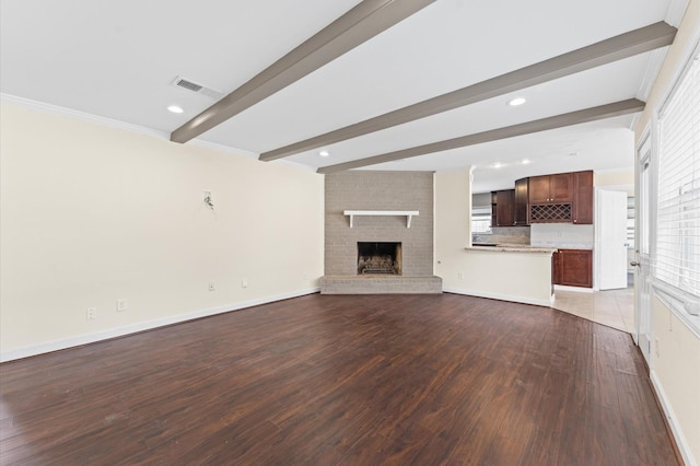 unfurnished living room with beam ceiling, a wealth of natural light, visible vents, and wood finished floors